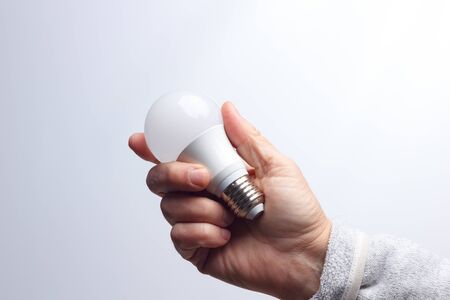 Energy saving daylight bulb, in the hand of an adult; bulb prepared to be installed and connected to...