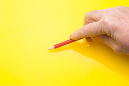 Wooden pencil with the interior of color and the exterior of the same color as in its interior, held in the hand of a person and on a colored backgroundの写真素材