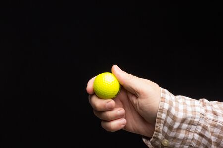 Yellow golf ball on a black background, in the hand of an adult person.の写真素材