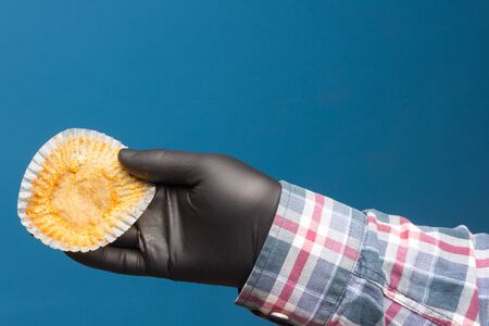 Industrial cupcake in the hand disinfected and protected with a black glove, on a blue background....