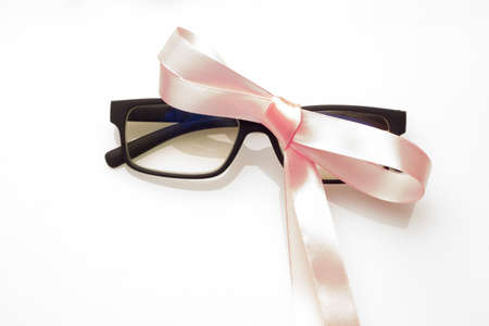 Glasses with graduated glasses and black frame, classic plastic on white background and red gift ribbonの写真素材