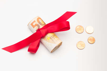 Roll of Euro banknotes surrounded by a red ribbon and a pretty bow. Colorful ribbon surrounding euro banknotes. Give money as a gift. To donate to an NGO is to make a good gift to those who need it.の写真素材