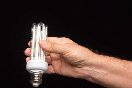 Energy saving bulb, on a black background and in the hand of an expert installer, ready to be installed.の写真素材