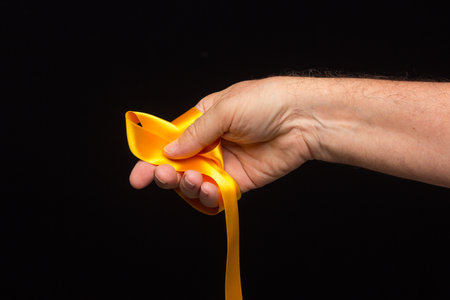 yellow ribbon in the palm of the hand on a black background; preparing the ribbon for wrapping a...