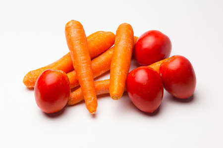 Red and orange tomatoes and carrots on a white backgroundの写真素材