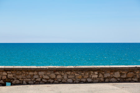 Stone wall overlooking tranquil blue sea under clear sky, creating serene coastal landscapeの写真素材