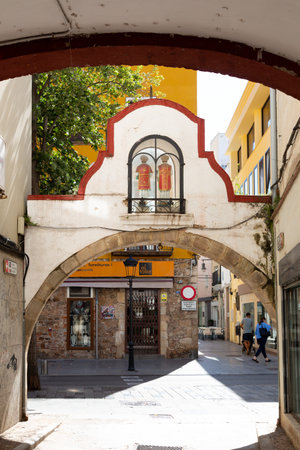 Plants are flanking a narrow street leading to an archway in a Spanish townの写真素材