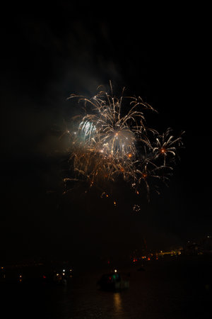 Bright fireworks exploding over boats on the water illuminating the night skyの写真素材