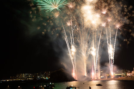 Bright fireworks exploding over boats on the water illuminating the night skyの写真素材