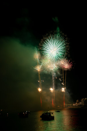 Bright fireworks exploding over boats on the water illuminating the night skyの写真素材