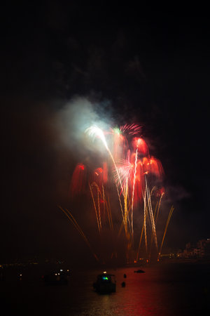 Bright fireworks exploding over boats on the water illuminating the night skyの写真素材