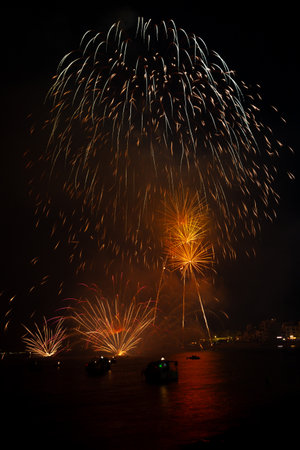 Bright fireworks exploding over boats on the water illuminating the night skyの写真素材