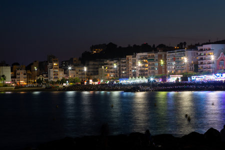 Tourists and locals are enjoying a summer night on the beach, watching a festival with amusement rides and live musicの写真素材