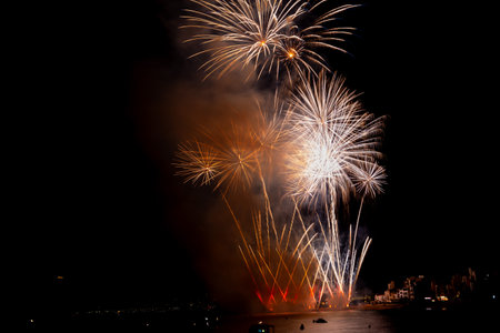 Bright fireworks exploding over boats on the water illuminating the night skyの写真素材