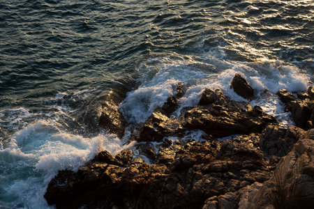 White ocean waves crashing on dark rocks on a sunny day