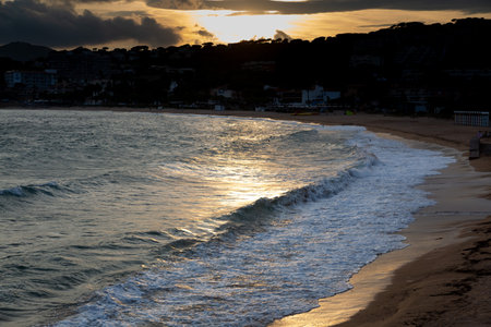 Soft waves reflecting golden sunset light gently lapping a sandy beach at dusk
