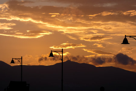 Street lamps create silhouettes against a beautiful sunset sky filled with colorful cloudsの写真素材