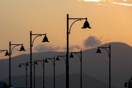 Street lamps create silhouettes against a beautiful sunset sky filled with colorful cloudsの写真素材