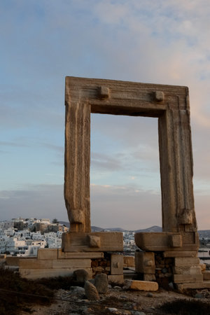 The ancient Portara, a marble doorway, stands on the islet of Palatia in Naxos, Greece, offering stunning views of the Aegean Sea and the town of Chora at sunsetの写真素材