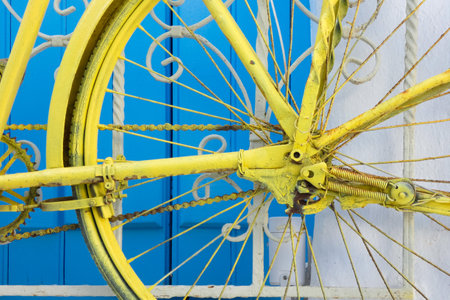 Close-up of a rusty yellow bicycle hanging on a blue and white gate, creating a vibrant contrastの写真素材