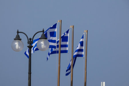National flag of Greece waving on flagpole on sunny day with blue sky and some cloudsの写真素材