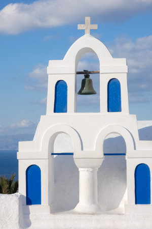 Picturesque white church with blue dome overlooking the Aegean sea with sailboats on a sunny day in Santorini, Greeceの写真素材