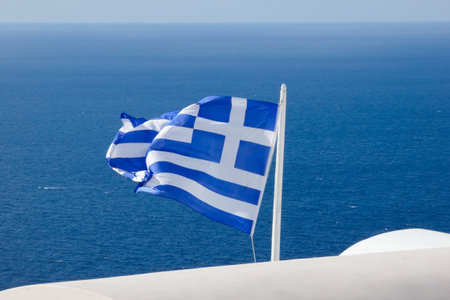 National flag of Greece waving on flagpole on sunny day with blue sky and some cloudsの写真素材