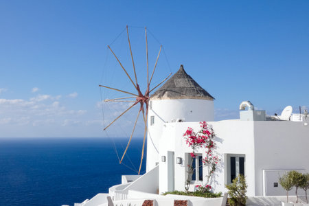 Picturesque whitewashed windmill standing tall against a vibrant blue sky, showcasing traditional Greek architecture and island charmの写真素材