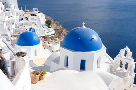 Picturesque white church with blue dome overlooking the Aegean sea with sailboats on a sunny day in Santorini, Greeceの写真素材