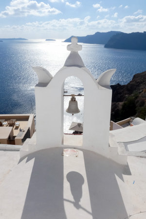 Picturesque white church with blue dome overlooking the Aegean sea with sailboats on a sunny day in Santorini, Greeceの写真素材