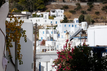 Traditional whitewashed houses with blue accents cover a hillside in a charming Greek village, creating a serene and picturesque sceneの写真素材