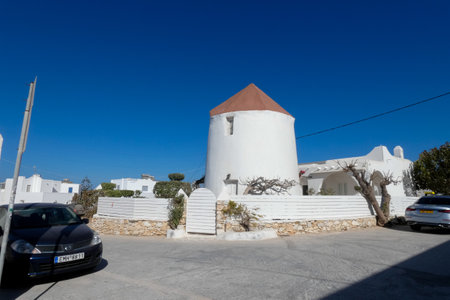 Picturesque whitewashed windmill standing tall against a vibrant blue sky, showcasing traditional Greek architecture and island charmの写真素材