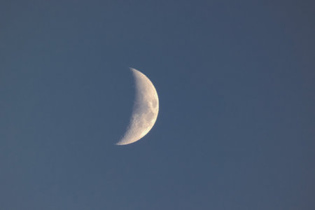 Waxing crescent moon with visible craters in the daytime skyの写真素材