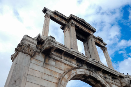 Low angle view of the roman agora gate showing its weathered columns and detailed architecture against a cloudy sky in Athensの写真素材