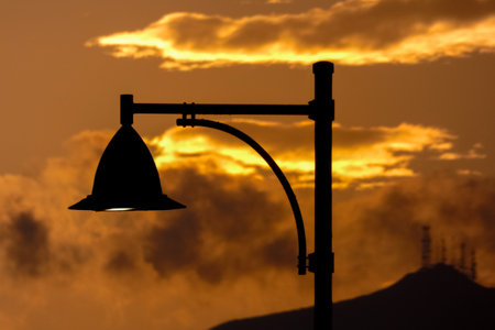 Street lamps create silhouettes against a beautiful sunset sky filled with colorful cloudsの写真素材