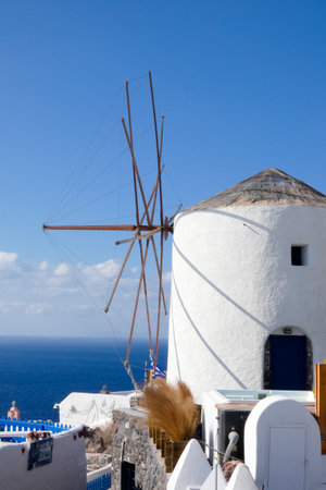 Picturesque whitewashed windmill standing tall against a vibrant blue sky, showcasing traditional Greek architecture and island charmの写真素材