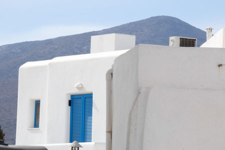 Traditional Greek architecture featuring a whitewashed building with blue shutters, set against a mountainous backdrop, evokes a sense of tranquility and Mediterranean charmの写真素材