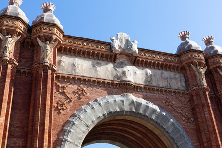 Arc de triomf, a triumphal arch built of red brick, showcases intricate details and sculptures against a clear blue sky in Barcelonaの写真素材