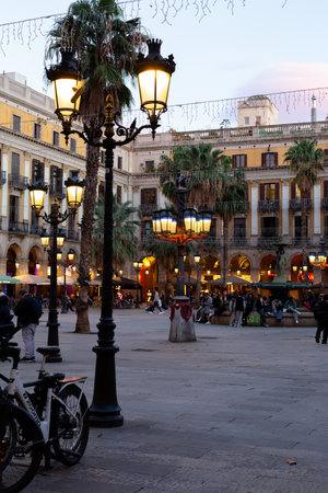 Ornate streetlights illuminating plaÃ§a reial at dusk with tourists and locals enjoying the evening in Barcelona, Spainの写真素材