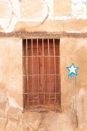 Rusty metal bars protecting a closed brown window of an old grungy wall with graffiti