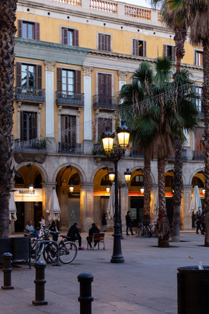 Ornate streetlights illuminating plaÃ§a reial at dusk with tourists and locals enjoying the evening in Barcelona, Spainの写真素材