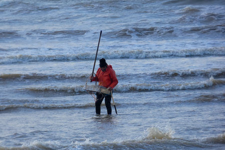 Fisherman wearing orange jacket pushing his shrimp net in the ocean waves