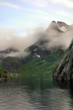 Norwegian fjord surrounded by high mountains with clouds and snowの写真素材