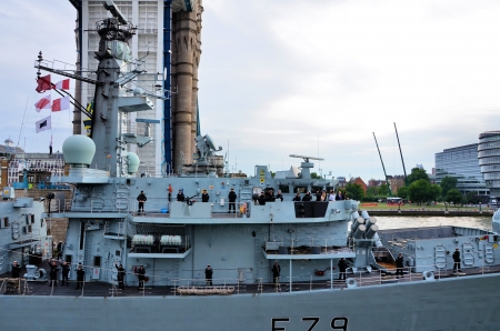 Battleship with the crew profiled passing next to Tower Bridgeのeditorial素材