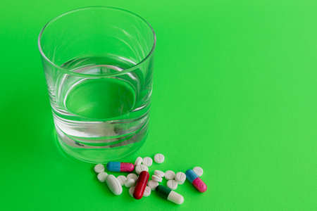 Medicine capsules and glass of water on green backgroundの写真素材