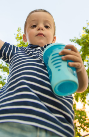 Serious child looking down with a bottle in handの写真素材