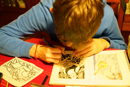 A boy is drawing a picture of a woman on a red table. He is using a pencil and a red crayonの写真素材
