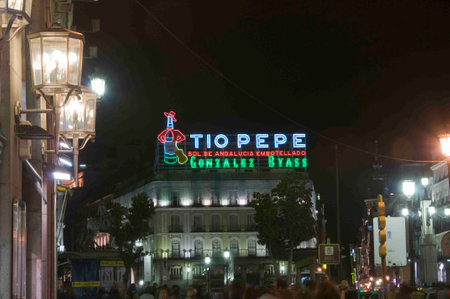 A vibrant night shot featuring the iconic "Tio Pepe" neon sign glowing against the dark sky. The sign illuminates the surrounding historic buildings, creating a nostalgic and lively atmosphere in the heart of the city.の写真素材