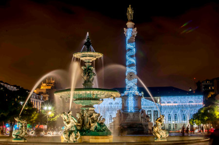 Night view of a beautifully illuminated fountain and monument in a city square, with decorative lights and statues, creating a festive atmosphere.の写真素材