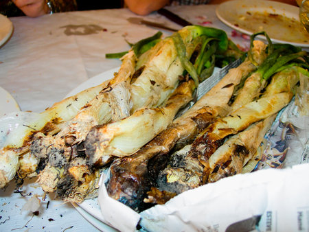 Calcots, a type of green onion, freshly grilled and wrapped in newspaper, ready for a traditional Catalan calcotadaの写真素材
